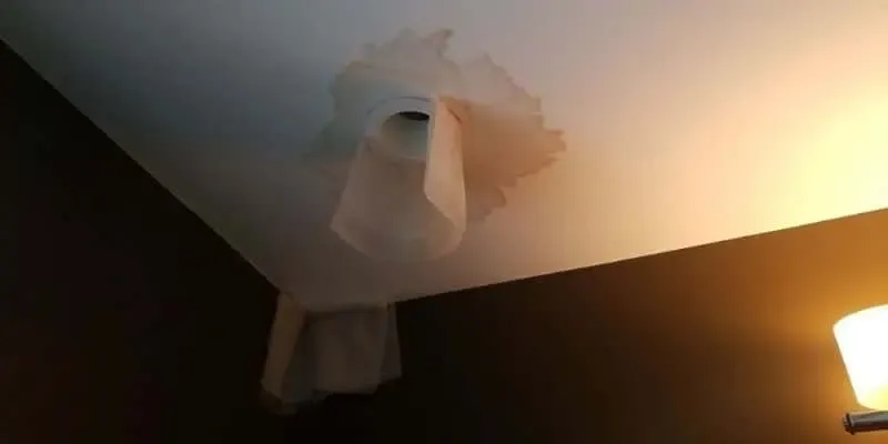 Bulging, peeling ceiling paint and plaster around a leak in a softly lit room