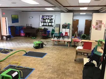 Drying mats and air movers spread across a parquet floor in a wide, open room